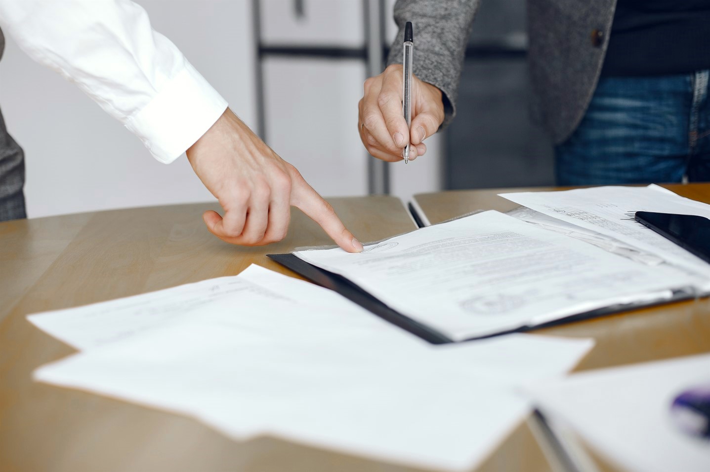 Una mano señala un documento mientras otra mano acerca un bolígrafo para firmar